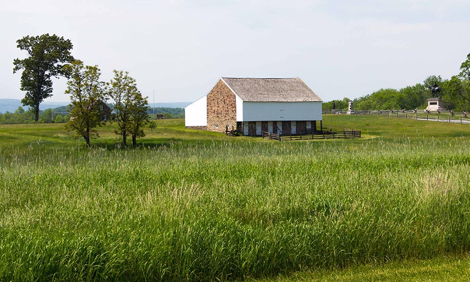 A scenic view of a rustic barn surrounded by tall grass and trees on a clear day.